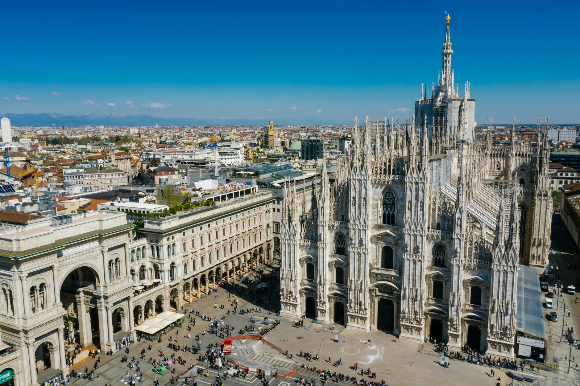 aerial view of Milan Duomo and Galleria Vittorio Emanuele II rooftops at golden hour with Alps in distance