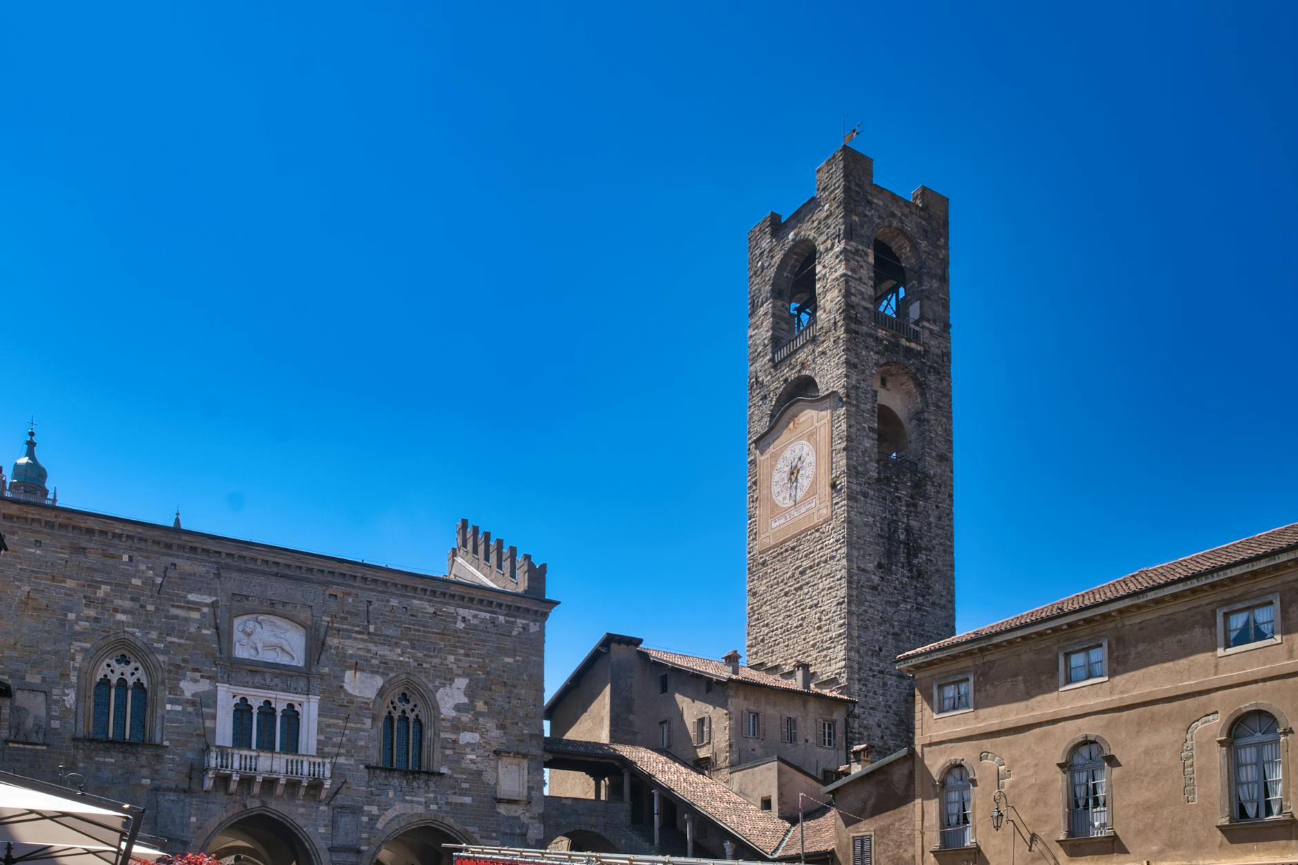 Bergamo Alta Piazza Vecchia with medieval stone tower and outdoor cafe tables in afternoon light