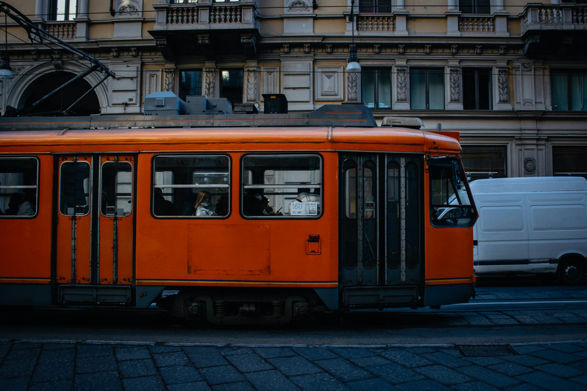 Orange 1928 Carrelli tram on cobblestone street with historic Milan facade in background