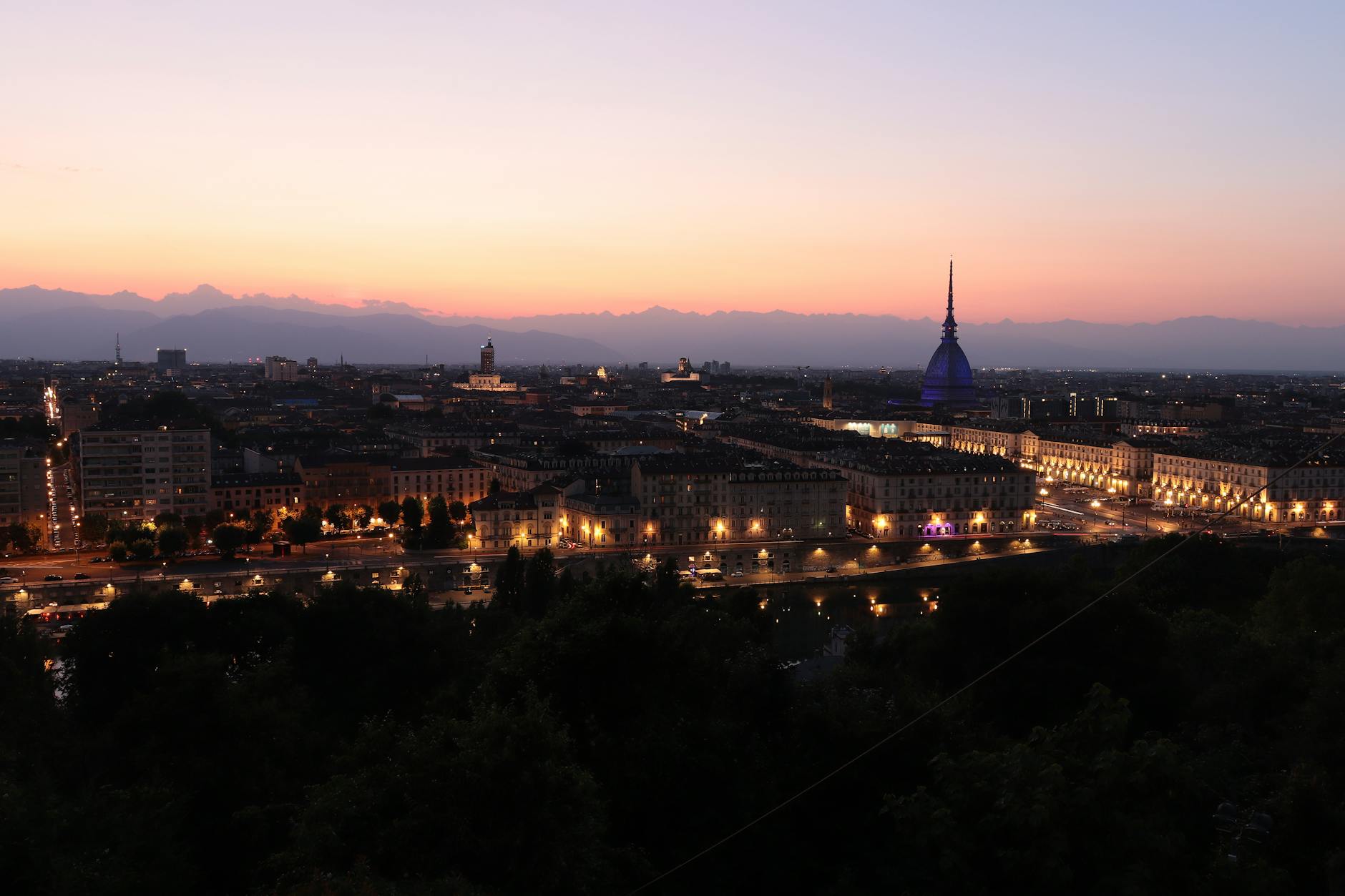 Sunset view of the Mole Antonelliana tower above Turin's rooftops with the Alps visible in the distance