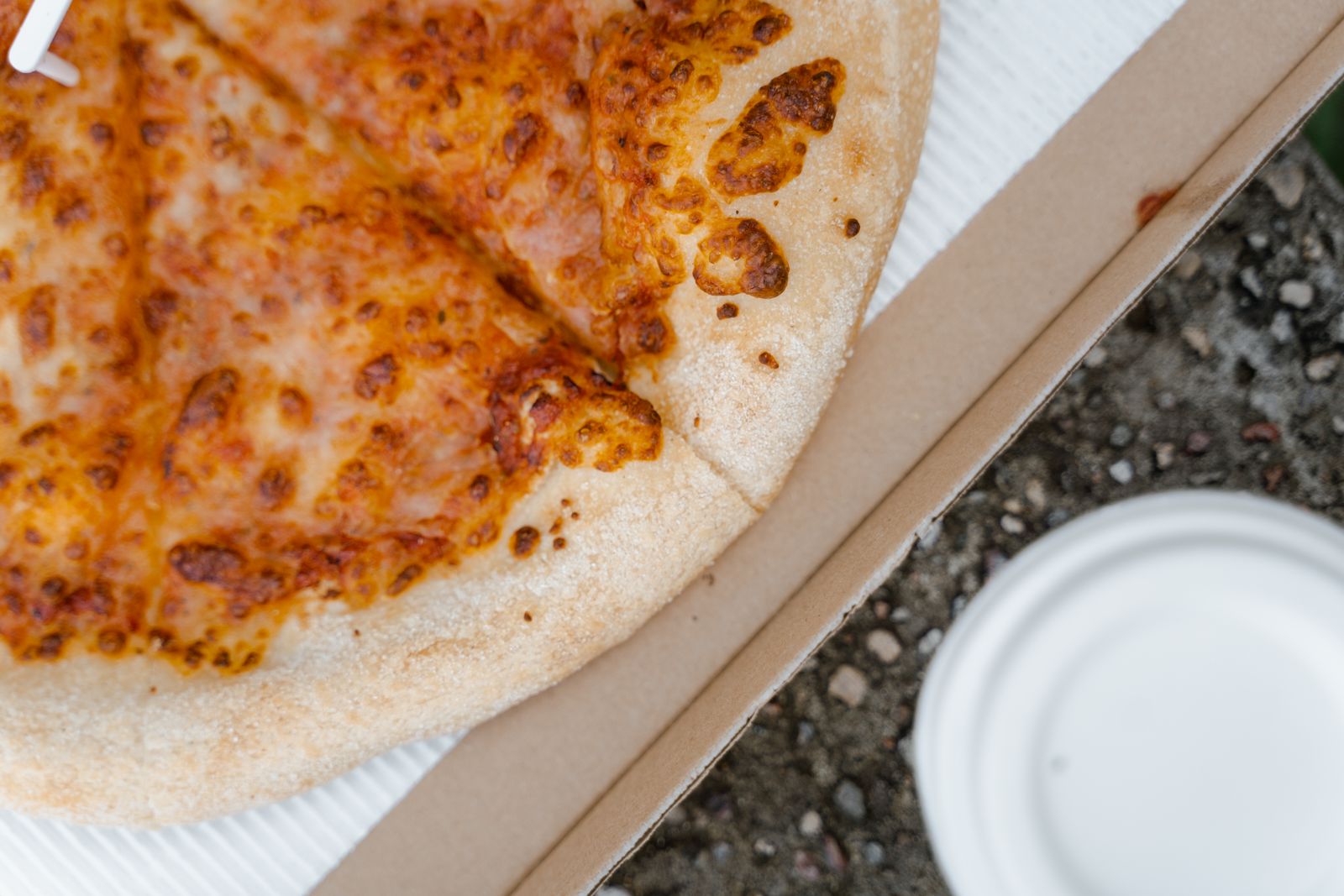 A cheesy slice of pizza al taglio in a cardboard tray, one of the best-value cheap lunches in Milan