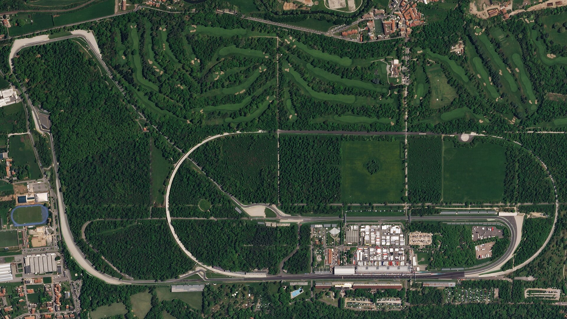 Satellite view of the Autodromo Nazionale Monza showing the modern circuit and the abandoned banked oval running through the wooded parkland, with the pit buildings and paddock alongside the main straight