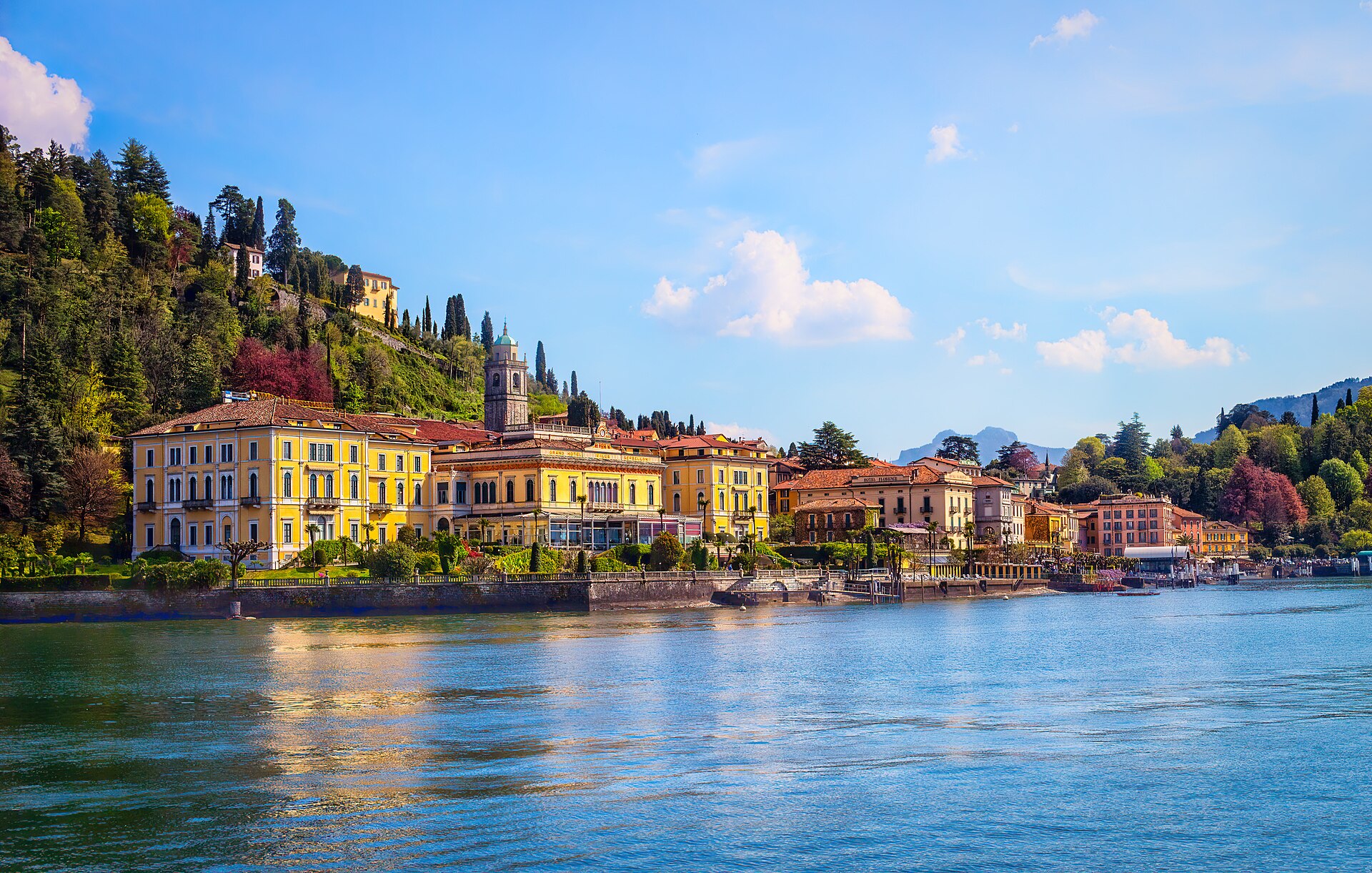 Bellagio seen from the water, with pastel waterfront buildings stacked up the promontory and wooded hills rising behind