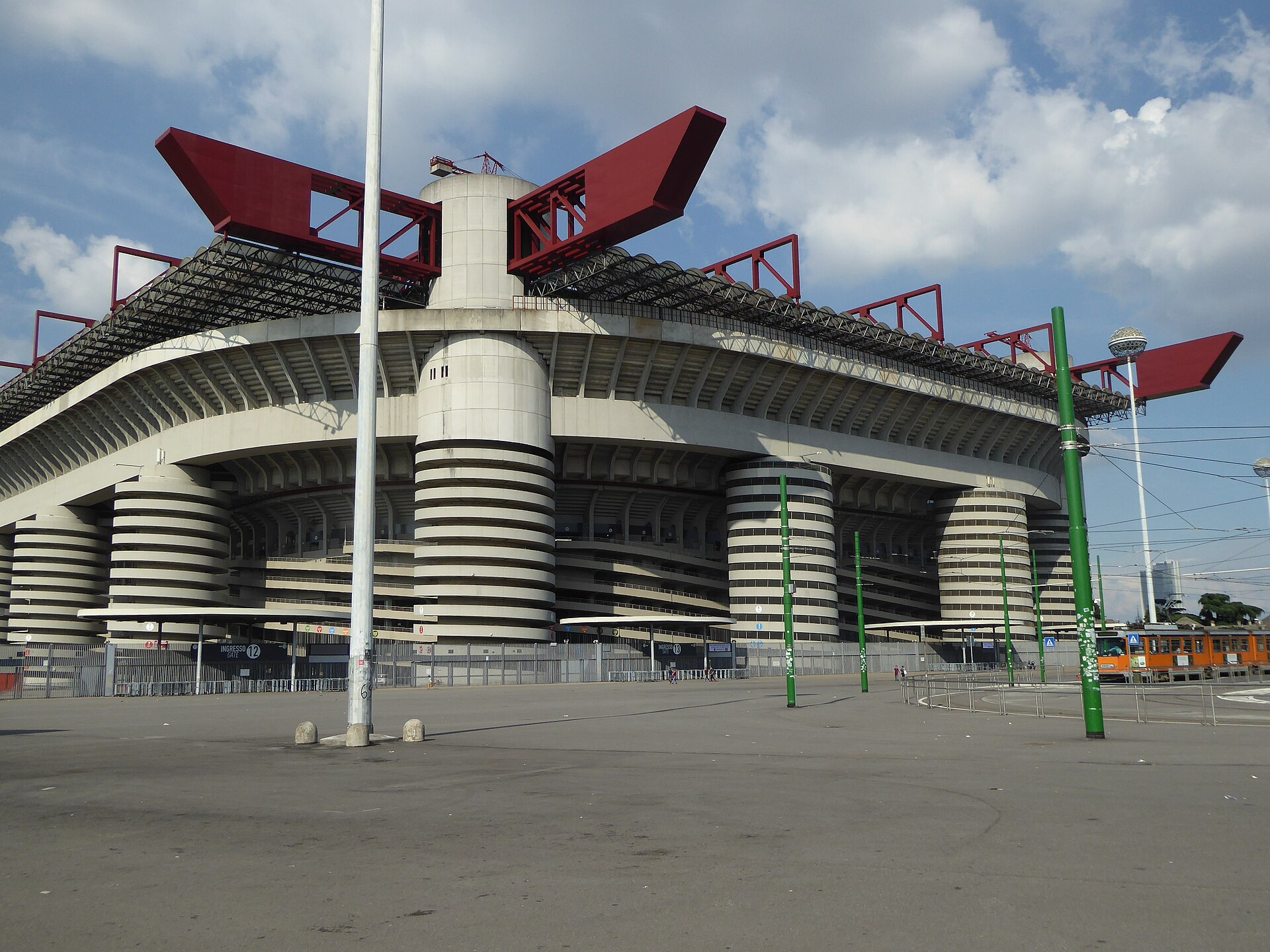 The exterior of San Siro stadium in Milan, showing the concrete spiral access ramps and the dark red steel girders of the roof structure